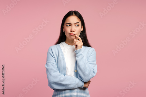 Young woman thinking hard keeping hand on chin posing on pink background, looking away photo