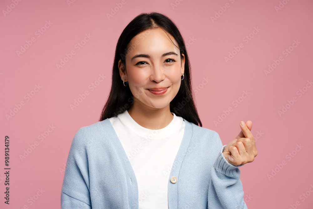 Smiling, attractive Asian woman making korean finger heart gesture on pink background