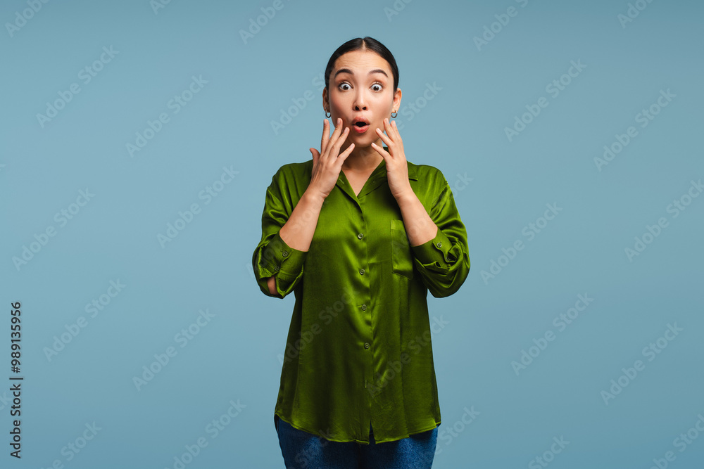 Shocked young woman holding her hands on cheeks posing isolated on blue background