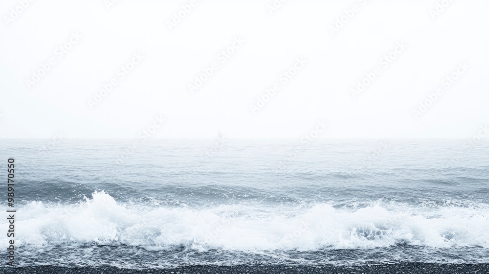 Fototapeta premium A beach covered in heavy fog, waves crashing violently, distant lighthouse barely visible