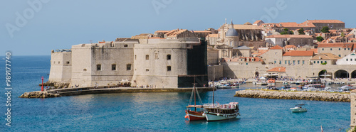 Visitors stroll along the iconic stone walls of Dubrovnik Croatia while colorful boats sway gently in the harbor under the bright blue sky