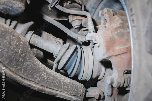 View from inside dirty used suspension of front-wheel drive car. Angle on CV joint with semi-drive and brake caliper