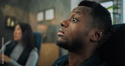 Close up of African American man listening his girlfriend during couples therapy. In the background, unfocused Asian woman talks, discusses relationship problem with therapist on counseling session.