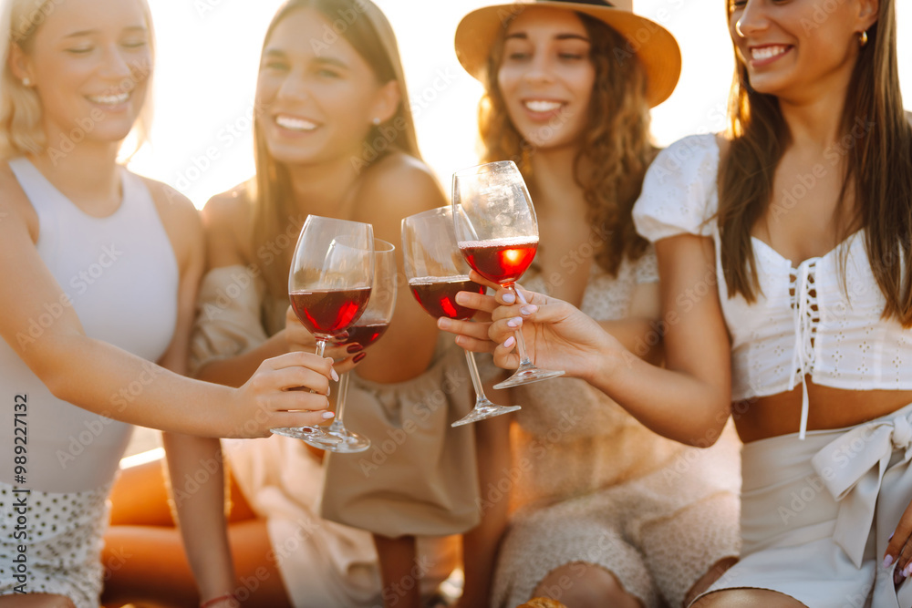 Four friends celebrate together at the beach, raising their glasses of red wine. The sun sets in the background, creating a warm and joyful atmosphere. Hen party. Four friends celebrate together at the beach, raising their glasses of red wine. The sun sets in the background, creating a warm and joyful atmosphere. Hen party.