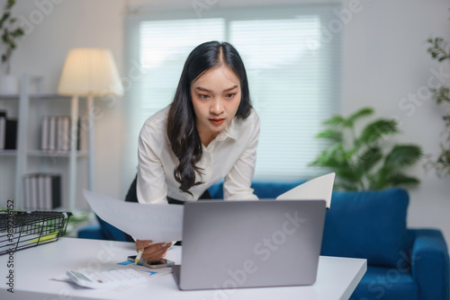 Businesswoman is standing in her home office leaning over her desk and reviewing paperwork photo