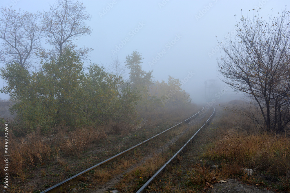 A dense white fog enveloped the autumn nature, trees, bushes and yellow-brown grass. Sand paths along the railway, metal railroad runs. A dense white fog enveloped the autumn nature, trees, bushes and yellow-brown grass. Sand paths along the railway, metal railroad runs.