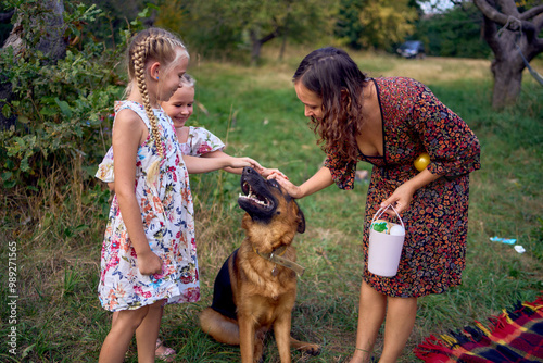 mom and little girls sisters playing with german shepherd dog during easter picnic in the garden photo