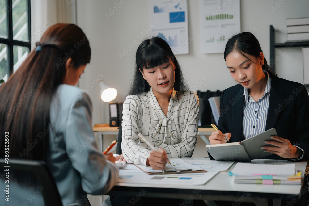 Three asian businesswomen are having a meeting in the office and analyzing financial documents using a calculator Three asian businesswomen are having a meeting in the office and analyzing financial documents using a calculator