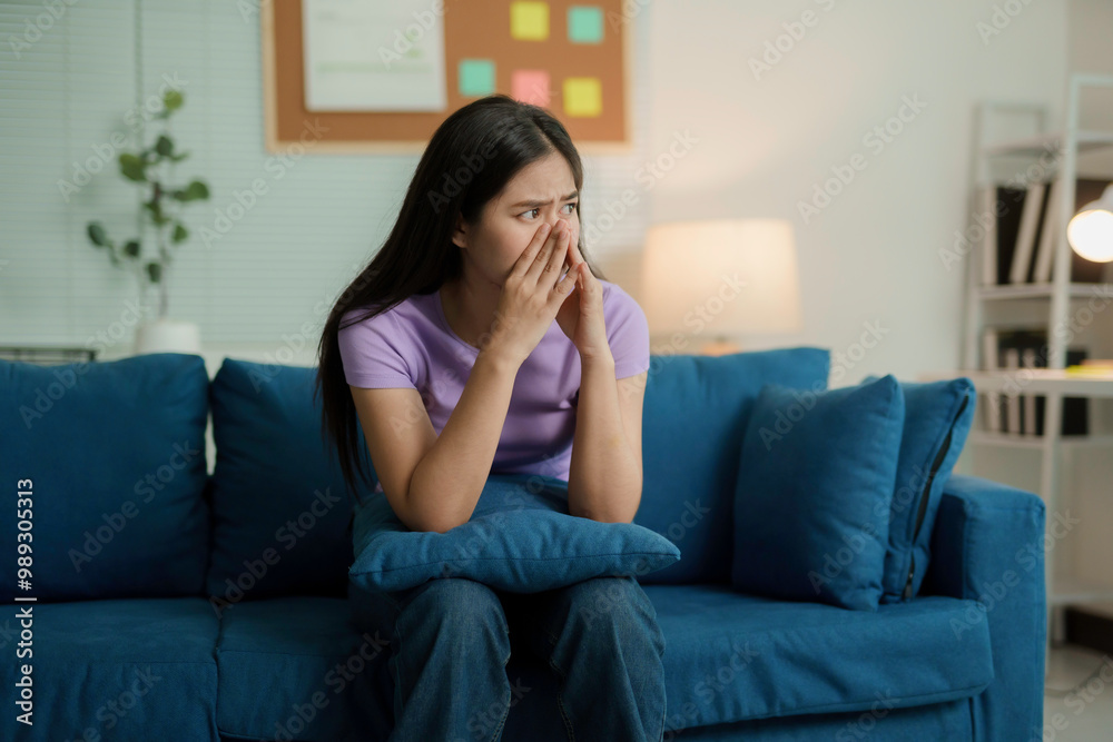 Young asian woman is covering her face with her hands and feeling sad while sitting alone on a blue sofa in the living room at night Young asian woman is covering her face with her hands and feeling sad while sitting alone on a blue sofa in the living room at night