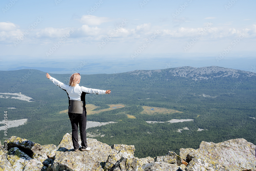 Obraz premium A person stands triumphantly on a mountain peak, arms spread wide in joy, reveling in the breathtaking beauty of the surrounding nature