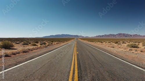 A long, open road extending through a dry landscape beneath a bright blue sky, perfect for travel and adventure themes.