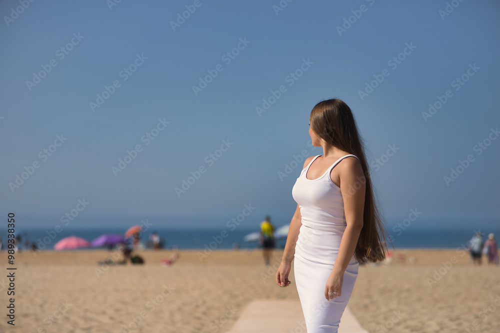 Young beautiful woman in a white dress, posing as a model on the beach with her back facing the sea. Concept beauty, fashion, trendy, femininity. Young beautiful woman in a white dress, posing as a model on the beach with her back facing the sea. Concept beauty, fashion, trendy, femininity.