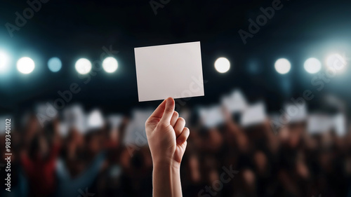 A hand holds a blank sign in front of a cheering crowd, with bright lights illuminating the scene, symbolizing expression and participation.