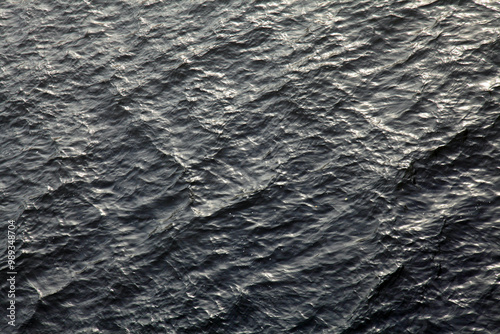 Gray wavy surface, texture, background. Dark water surface in late autumn with swell elements and mirror reflection of light sky. Abstract paints and sketches of water nature. Surrealistic palette