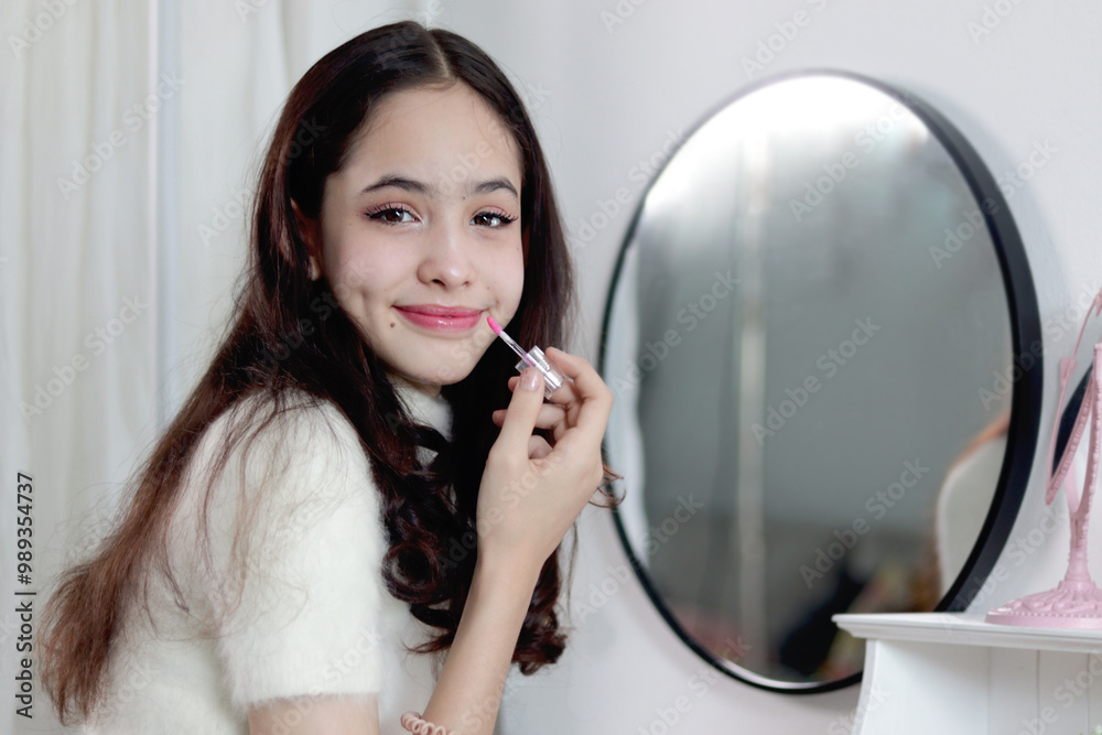 A beautiful teenage girl holding lipstick in front of a mirror and looking at camera, pretty young woman wearing makeup. Happy female teenager using cosmetics for beauty. A beautiful teenage girl holding lipstick in front of a mirror and looking at camera, pretty young woman wearing makeup. Happy female teenager using cosmetics for beauty.