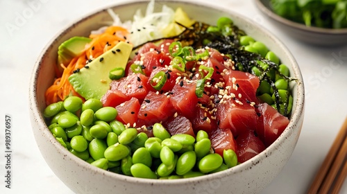 Closeup of a poke bowl with tuna, edamame, avocado, carrots, seaweed, sesame seeds, and green onions.