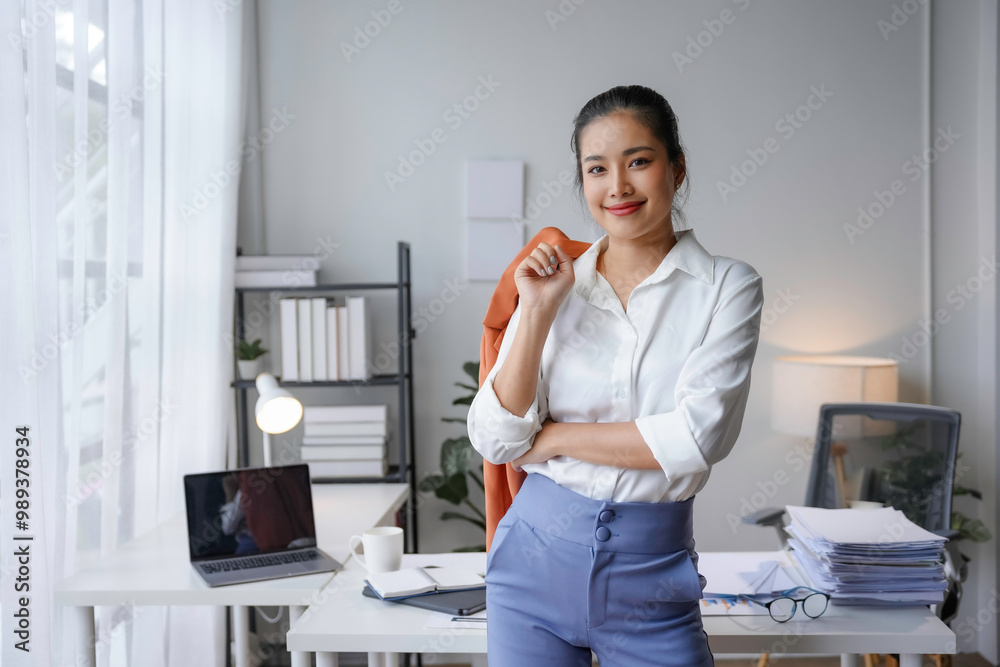 Asian businesswoman is holding her jacket and smiling while standing in her office Asian businesswoman is holding her jacket and smiling while standing in her office