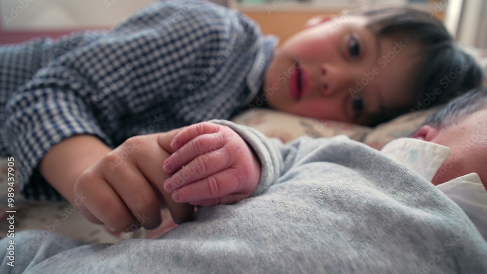 Young boy gently holding newborn sibling’s hand while lying side by side on a bed, capturing a moment of deep connection and affection between siblings in a warm and loving family Young boy gently holding newborn sibling’s hand while lying side by side on a bed, capturing a moment of deep connection and affection between siblings in a warm and loving family