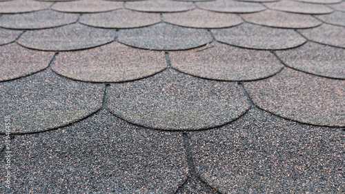 fragment of soft tile roof covering with granular texture and rounded edge lines in gray-red shade, background industrial textured surface photo