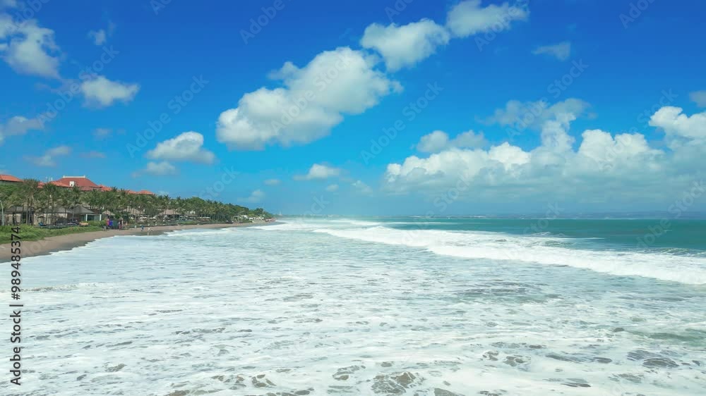 Aerial view of Seminyak beach in Bali with waves crashing onto the shore under a partly cloudy sky. Aerial view of Seminyak beach in Bali with waves crashing onto the shore under a partly cloudy sky.