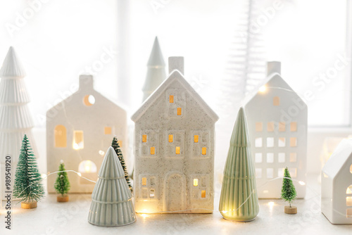 Christmas little ceramic houses, white snowy trees and golden lights on window. Xmas background. Merry Christmas! Atmospheric Christmas scene, miniature holiday village