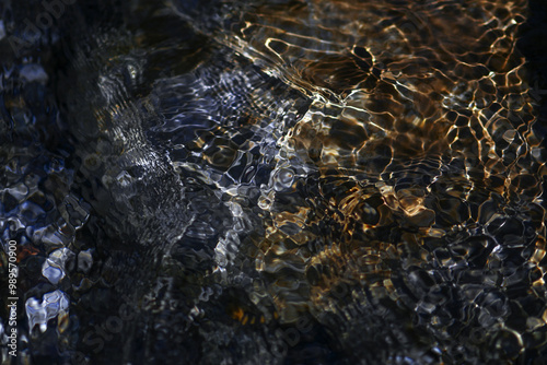 Clean water surface in a mountain stream river. Abstract of water surface in slow motion and pebbles at the bottom