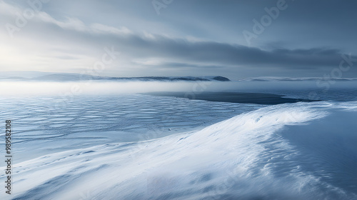 Obraz na płótnie A snowy hilltop overlooking a frozen lake with low clouds hanging over the horizon and the wind sweeping across the snow creating ripples and patterns. w salonie