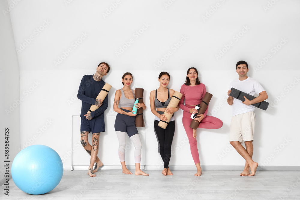 Naklejka premium Group of sporty young people with yoga mats and water bottles in gym