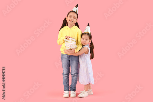 Wallpaper Mural Cute little Asian happy sisters in party hats with gift box on pink background Torontodigital.ca
