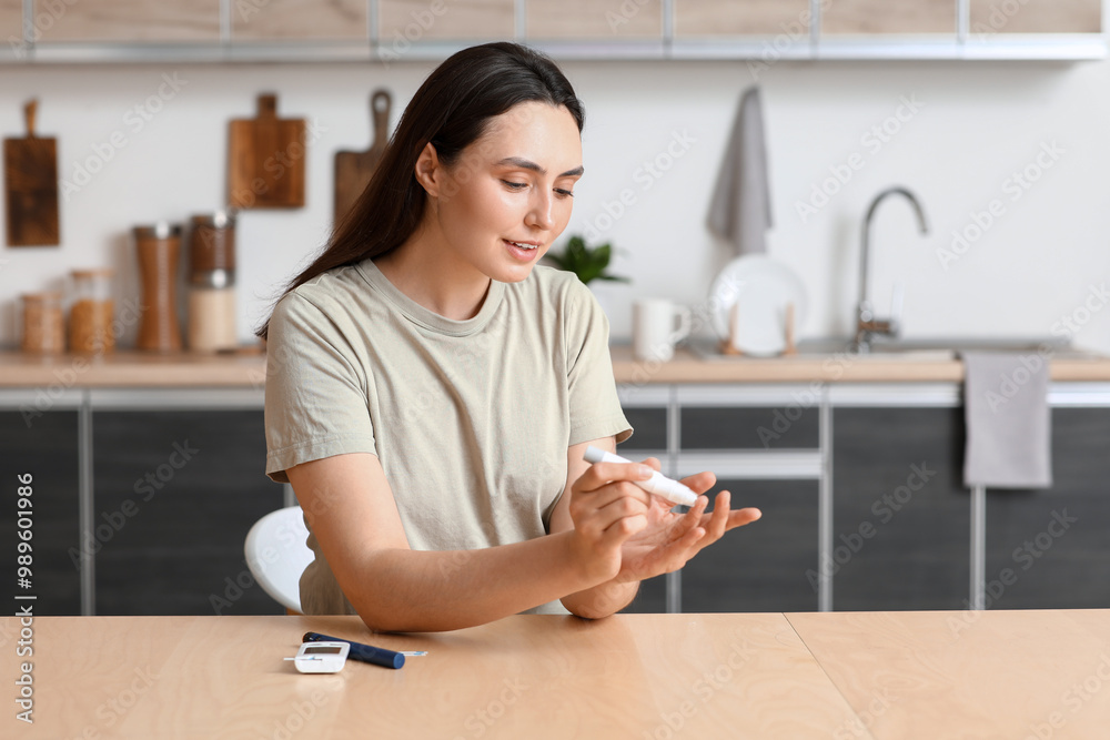 Diabetic young woman using lancet pen at table in kitchen Diabetic young woman using lancet pen at table in kitchen
