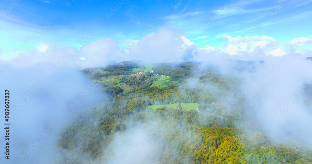 AERIAL: Small hilltop village in rural Slovenia hides under the white autumn cloud cover. Cinematic flying view of the picturesque fall colored countryside under the cloudy sky. Idyllic landscape AERIAL: Small hilltop village in rural Slovenia hides under the white autumn cloud cover. Cinematic flying view of the picturesque fall colored countryside under the cloudy sky. Idyllic landscape