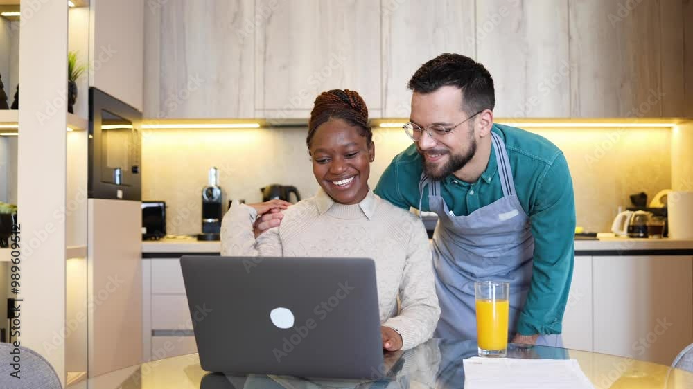 Cheerful mixed-race couple sharing a laptop while relaxing at home Cheerful mixed-race couple sharing a laptop while relaxing at home