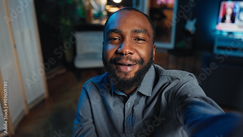 Smiling influencer using mobile phone to do live broadcast for subscribers, showing his home studio. Internet star films himself for viewership using POV camera, engaging with fans watching