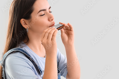 Tableau sur toile Young woman playing harmonica on light background, closeup