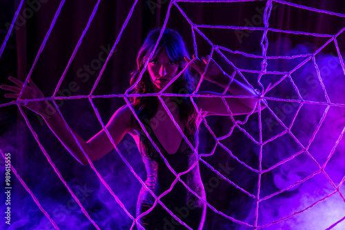 fit athletic brunette female wearing lingerie dress behind a spooky halloween spinder web with pink and purple colored smoke photo