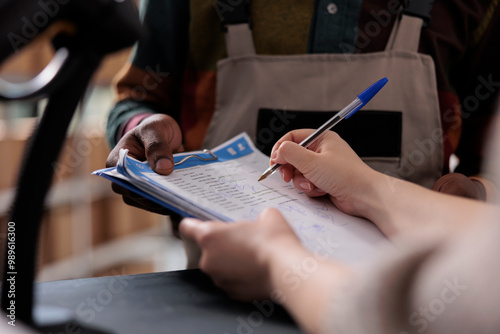 Storage room supervisor signing logistics report, discussing merchandise inventory working at goods quality control. Diverse team preparing customers orders for shipping in warehouse. Close up photo