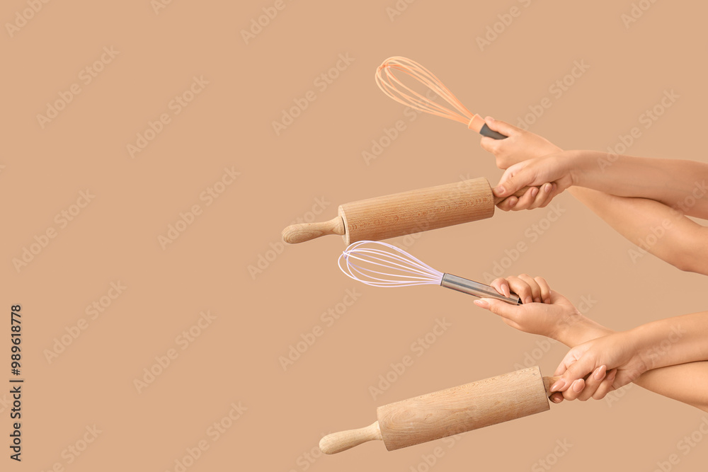 Female hands with rolling pins and whisks on beige background Female hands with rolling pins and whisks on beige background