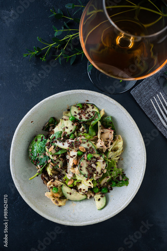 Fresh salad with cucumbers, lettuce, spinach, green peas, flax seeds and pumpkin with a glass of white wine.