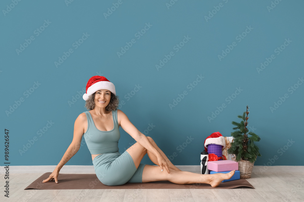 Obraz premium Sporty mature woman in Santa hat with Christmas gifts near blue wall
