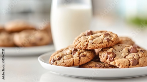 Stacked chocolate chip cookies on a plate with a glass of milk strategically placed in the background, emphasizing presentation and aesthetic appeal.