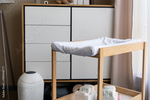 Empty nursery with changing table with diapers, lamp, commode and window with simple curtains