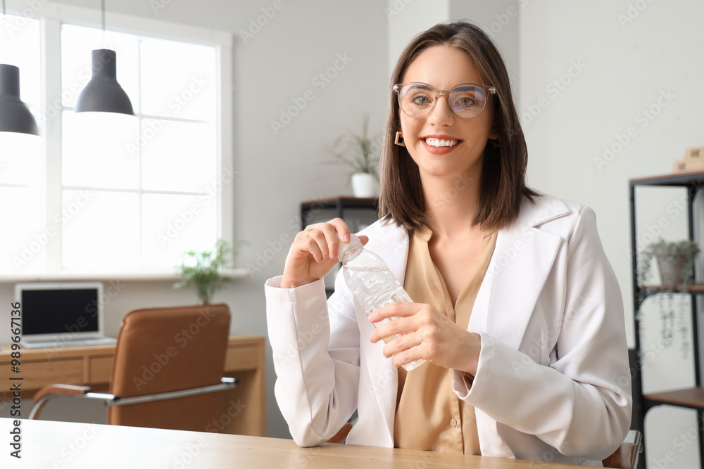 Young businesswoman with bottle of water video chatting at table in office Young businesswoman with bottle of water video chatting at table in office