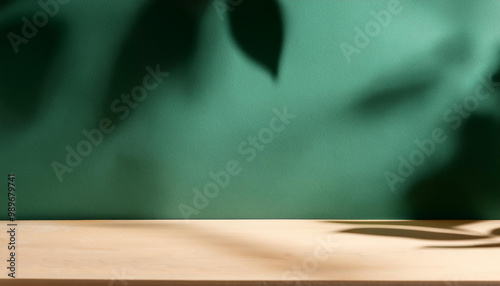 Empty table and darkgreen wall. Table with sun reflections and leaves shadows on beige wall. Background with bokeh for product photo