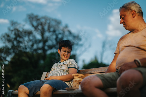 A father and son engage in a building blocks game on a park bench, enjoying quality time together outdoors.
