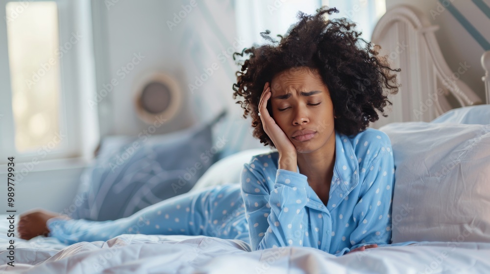 Sick biracial woman wearing blue pyjamas touching her head in bedroom Sick biracial woman wearing blue pyjamas touching her head in bedroom