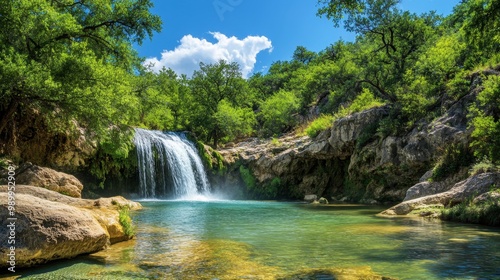 The gentle waterfall flows into a clear turquoise pool surrounded by lush green trees and large rocks under a bright, open sky
