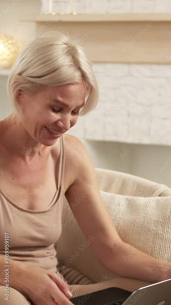 Vertical video. Virtual communication. Distance meeting. Cheerful casual woman talking in online conference on laptop sitting in cozy armchair at home.