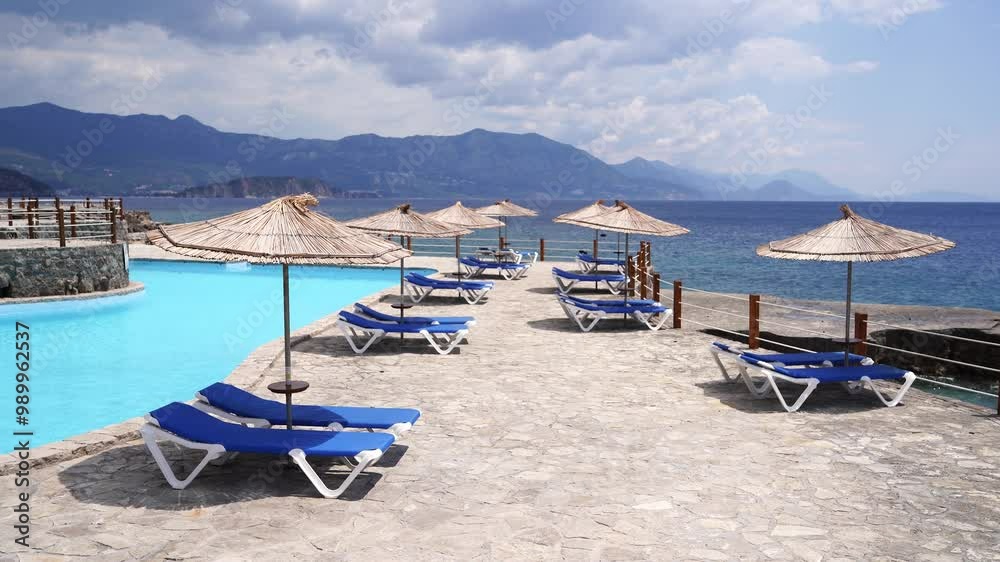 Wind shakes the straw umbrellas near the sun loungers near the pool by the sea. High quality 4k footage Wind shakes the straw umbrellas near the sun loungers near the pool by the sea. High quality 4k footage