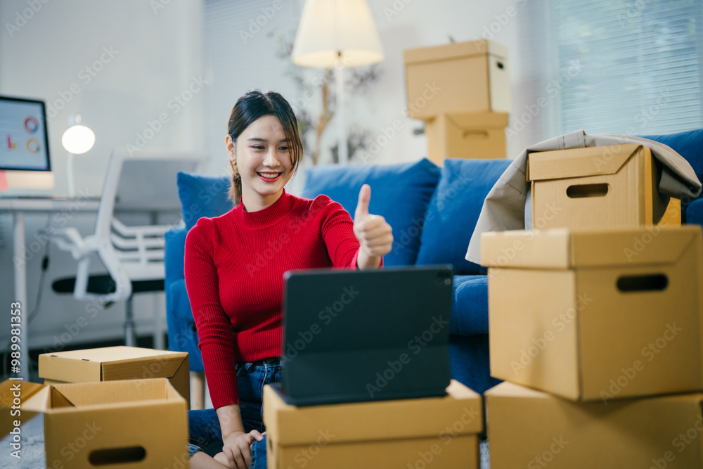 Excited asian woman in living room with moving boxes, smiling on tablet video call, showing thumbs up. Joy of new home and tech communication Excited asian woman in living room with moving boxes, smiling on tablet video call, showing thumbs up. Joy of new home and tech communication