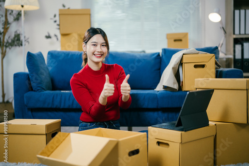 Fotografie Young woman is smiling and giving thumbs up while unpacking boxes in her new apartment